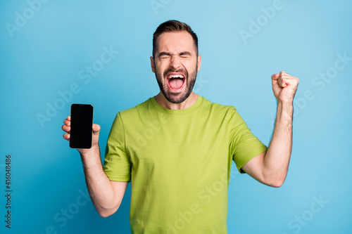 Photo of handsome cheerful man hold phone screen empty space win lucky isolated on blue color background