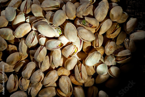 Pistachio texture close up. Nuts on a pile on a black wooden board. Contrasting dramatic light as an artistic effect.