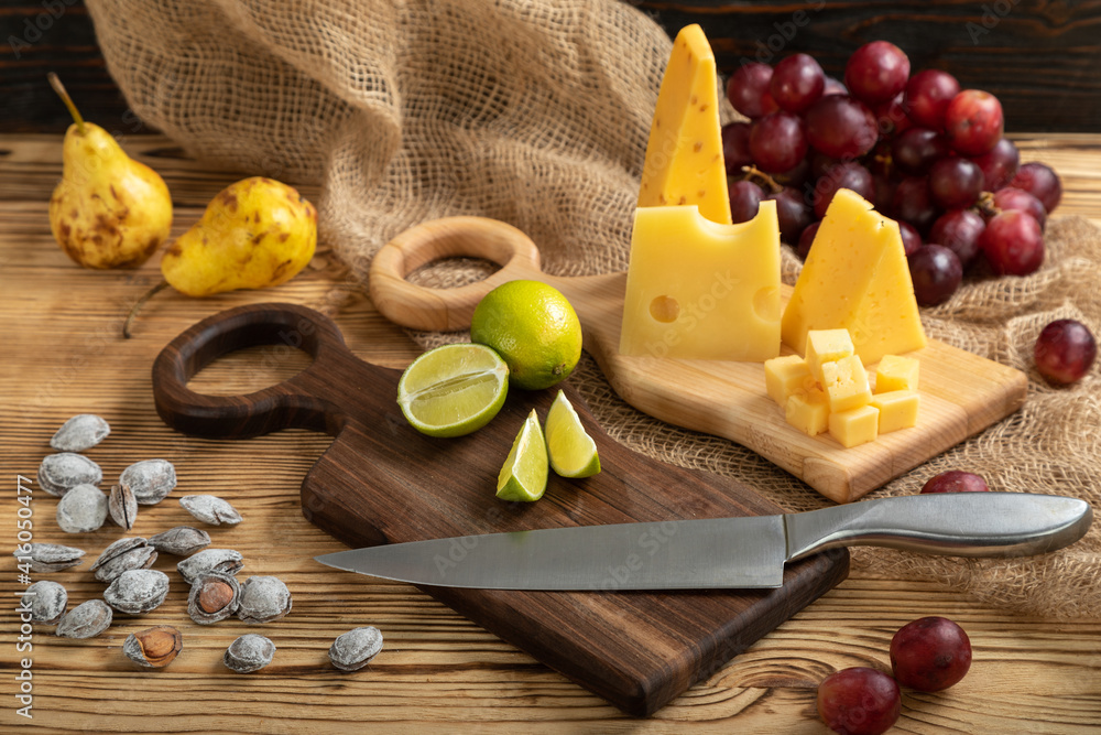 Cheese, grapes, lime, pear and nuts on a cutting board