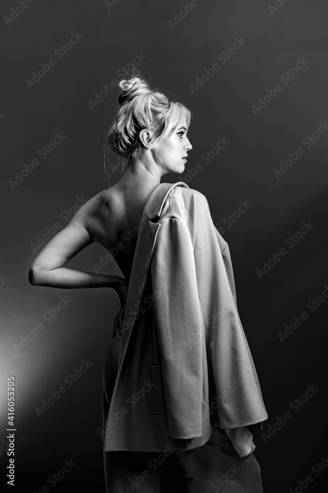 Portrait, softbox is visible in the frame. Sexy young blonde looking standing topless, a jacket hanging on his shoulder.
