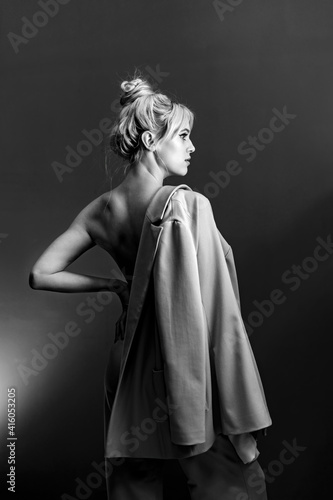 Portrait, softbox is visible in the frame. Sexy young blonde looking standing topless, a jacket hanging on his shoulder.
