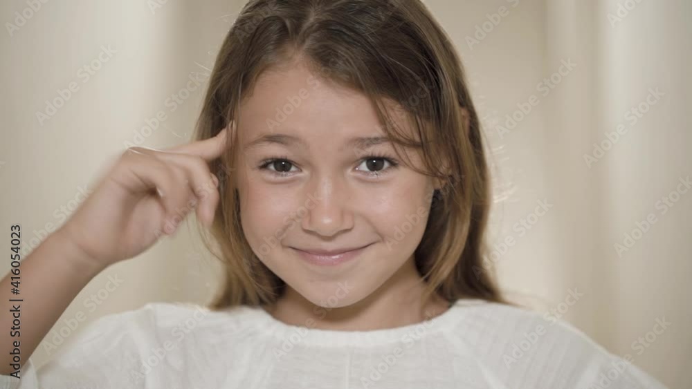 Close up girl child twists a finger at the temple looking at camera. She showing a screw-loose sign by twisting her finger into temple. Close up girl child twists a finger at the temple looking at camera. She showing a screw-loose sign by twisting her finger into temple.