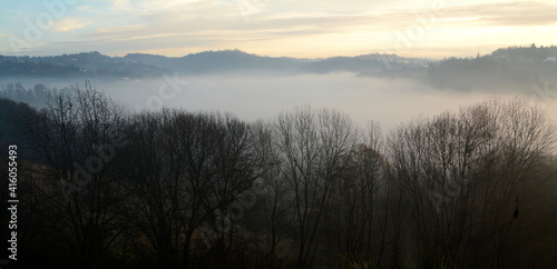 Autumn mists envelop a valley between hills and bare trees