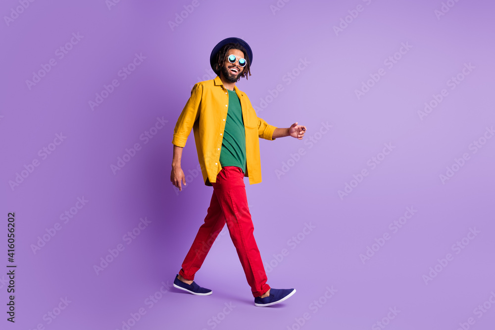 Full body profile portrait of cheerful dark skin person walking look camera isolated on purple color background Full body profile portrait of cheerful dark skin person walking look camera isolated on purple color background
