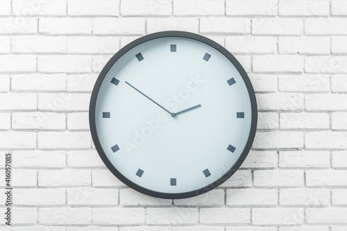 White round wall clock in black frame on light brick wall