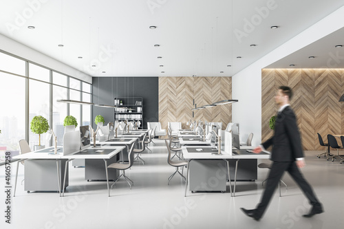 Blurry businessman silhouette in mosern light coworking office with light minimalistic furniture, wooden wall and big window photo