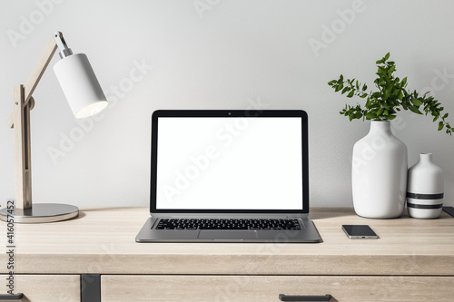 Front view on blank white laptop monitor on wooden table with decor elements for comfortable remote work. Mock up