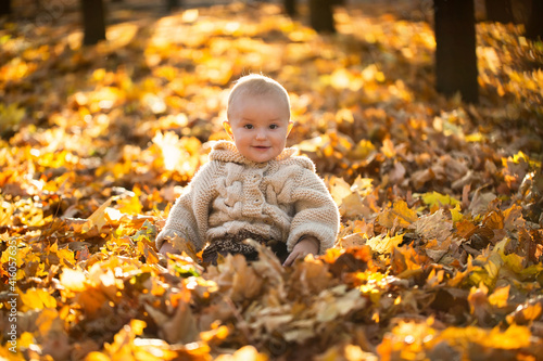 Small girl in a knitted suit is sitting in the forest in yellow leaves.