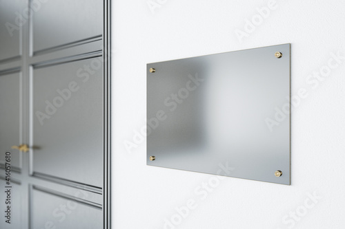 Blank metal signboard on white wall before the entrance a room with grey door. Mockup photo