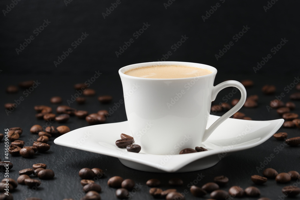 Close-up side view. White cup of coffee on a black background. Coffee beans on a black table. Close-up side view. White cup of coffee on a black background. Coffee beans on a black table.