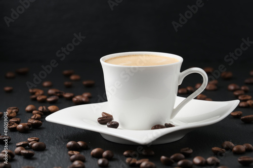 Close-up side view. White cup of coffee on a black background. Coffee beans on a black table.