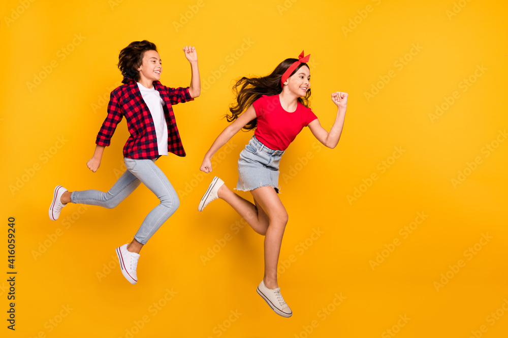 Full length profile portrait of two little energetic crazy pupils enjoy running isolated on yellow color background Full length profile portrait of two little energetic crazy pupils enjoy running isolated on yellow color background
