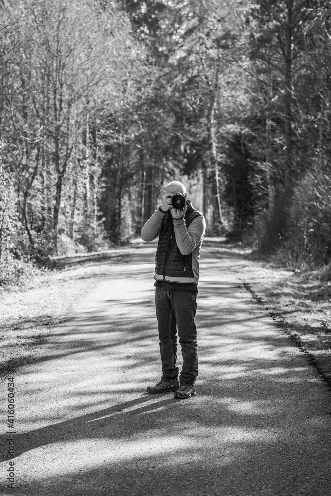a black and white photo of a photographer who stands in the forest of the swiss national park. a black and white photo of a photographer who stands in the forest of the swiss national park.
