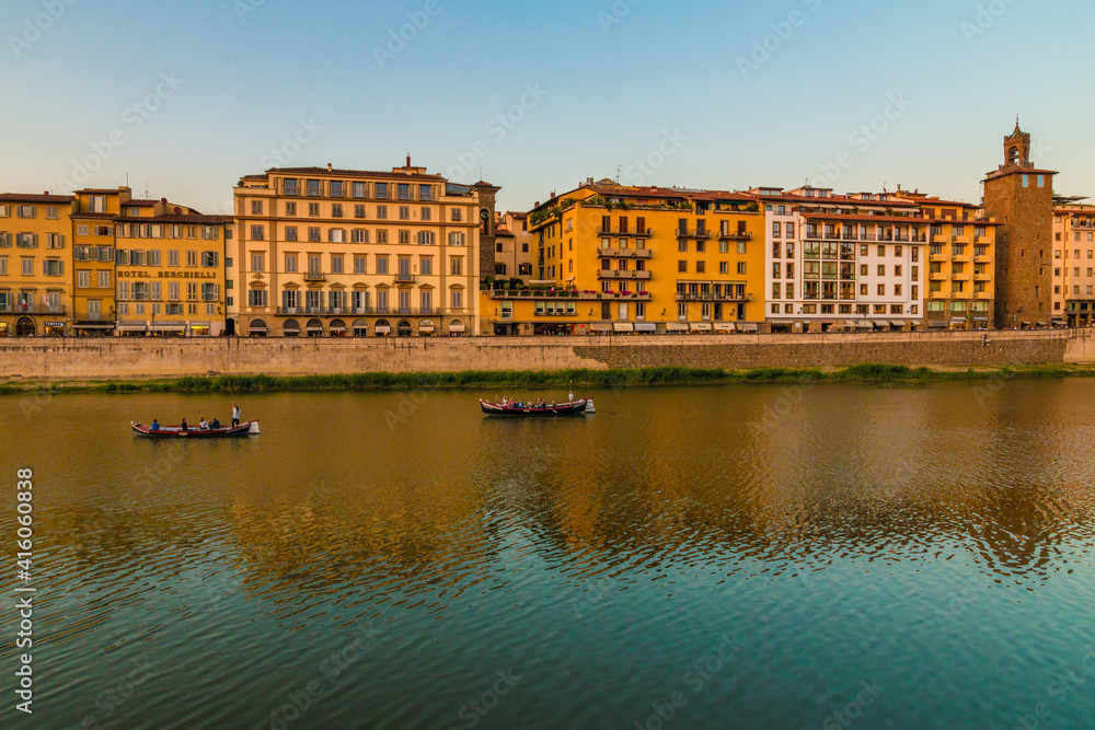Lovely Arno riverbank view along Lungarno degli Acciaiuoli street in Florence's historic city centre at dusk. Two vintage Florentine Gondola boats, so called Barchetto, are having a romantic cruise.