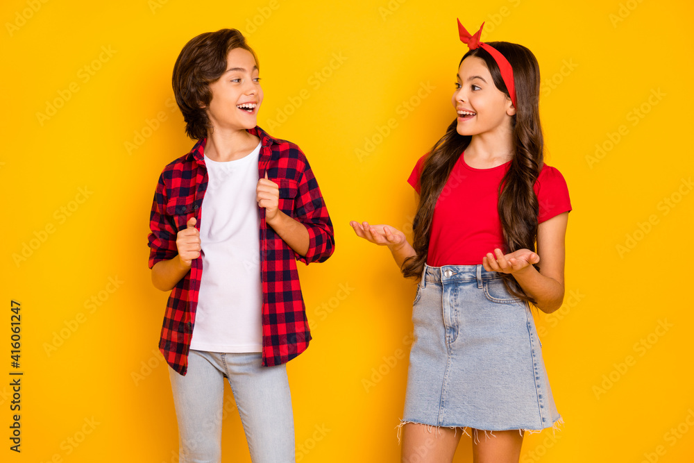 Portrait of positive boy girl look each other speak explain toothy smile isolated on yellow color background Portrait of positive boy girl look each other speak explain toothy smile isolated on yellow color background