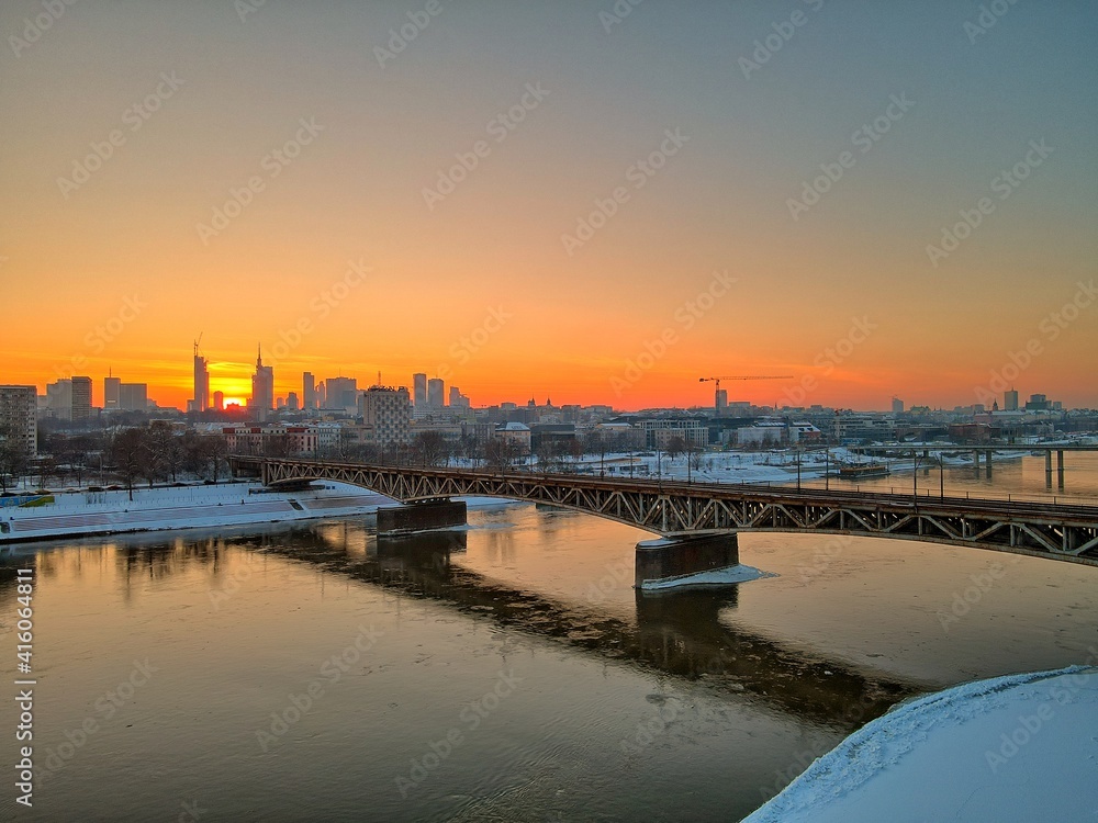 sunset view of the Vistula river and railway and road bridges and the sun setting over the center of Warsaw - aerial photography from a drone