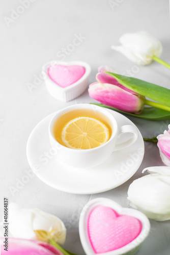 Tulips with white cup of tea on a light background. Spring tenderness still life composition with candles. Flowers for romantic, love atmosphere. Relax, meditation pause. Selective focus, copy space.