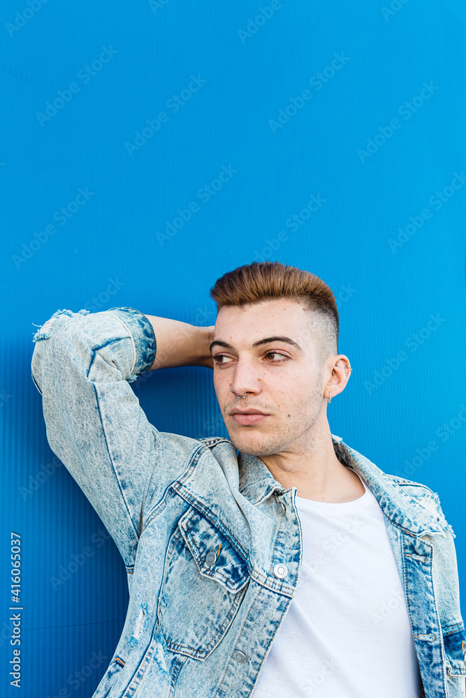 Obraz premium Portrait of an isolated young man looking confident and wearing a denim jacket in a blue background
