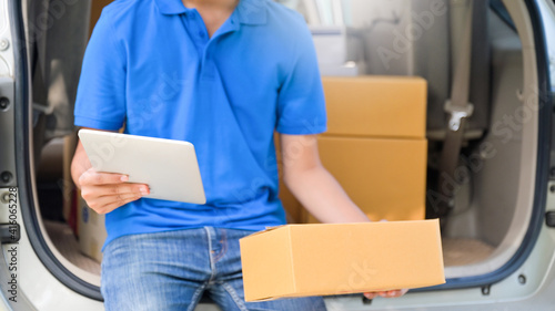 Delivery man sit at the car uses a tablet and holds a parcel box to deliver the goods to the customer.