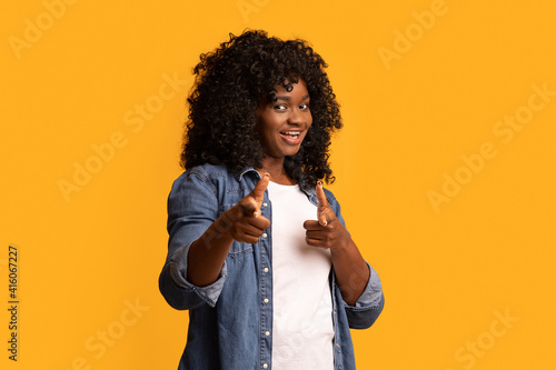 Cheerful black woman indicating at camera on yellow