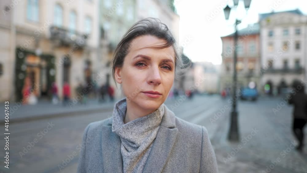 Portrait of a Caucasian woman in a coat in the middle of the old city square. She looking seriously at the camera. Slow motion Portrait of a Caucasian woman in a coat in the middle of the old city square. She looking seriously at the camera. Slow motion