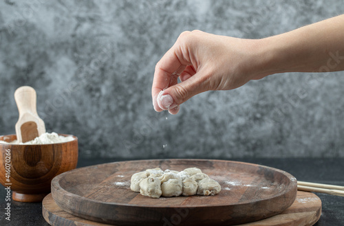 Hand taking a pinch of flour from a wooden bowl on a gray background