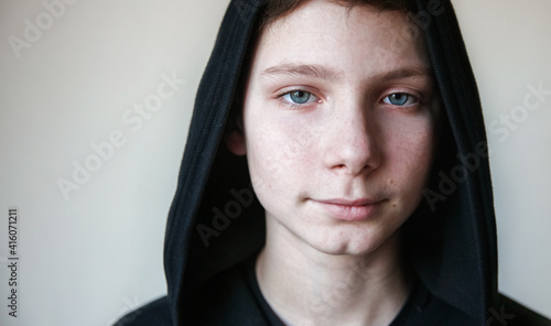 Portrait of a calm blue-eyed teenage boy in a black hood photo