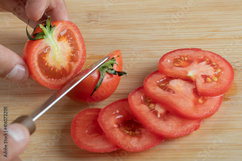 Hands cutting a fresh tomato on a wooden table