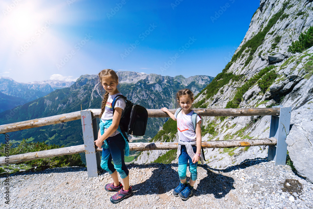 Children hiking on beautiful summer day in alps mountains Austria, resting on rock and admire amazing view to mountain peaks. Active family vacation leisure with kids. Outdoor fun and healthy activity