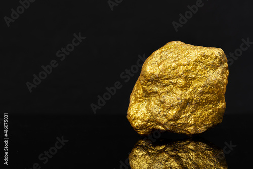 Investment sources on stock markets and financial concept: On right frame a single real raw gold piece on black shiny background with copy space and reflection. Measurement of wealth. Luxury jewelry