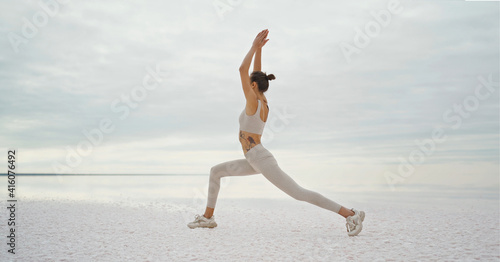 Slim body yoga woman doing exercise on salt lake coast with beautiful nature view, making warrior pose. Concept wellness and harmony