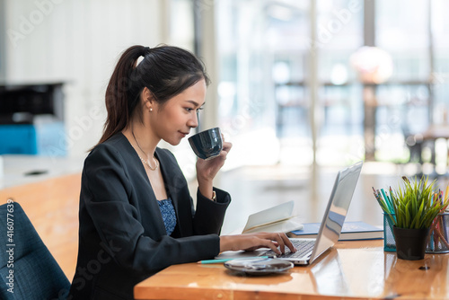 Side view of an Asian woman looking at her tablet Ready to drinking coffee in the office.