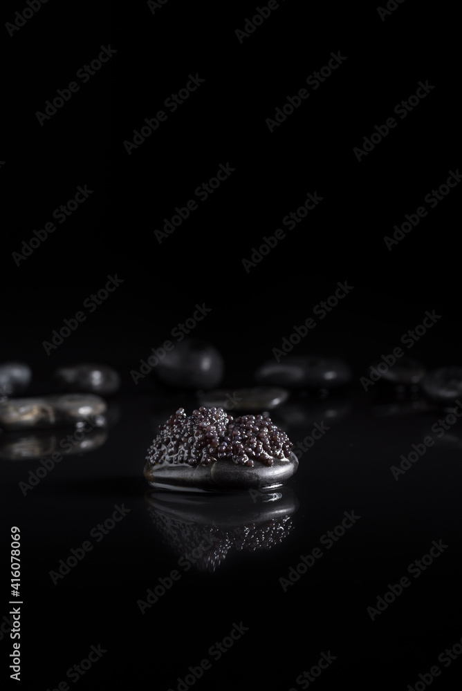 Caviar de esturión sobre piedra negra con reflejo en un fondo negro Caviar de esturión sobre piedra negra con reflejo en un fondo negro
