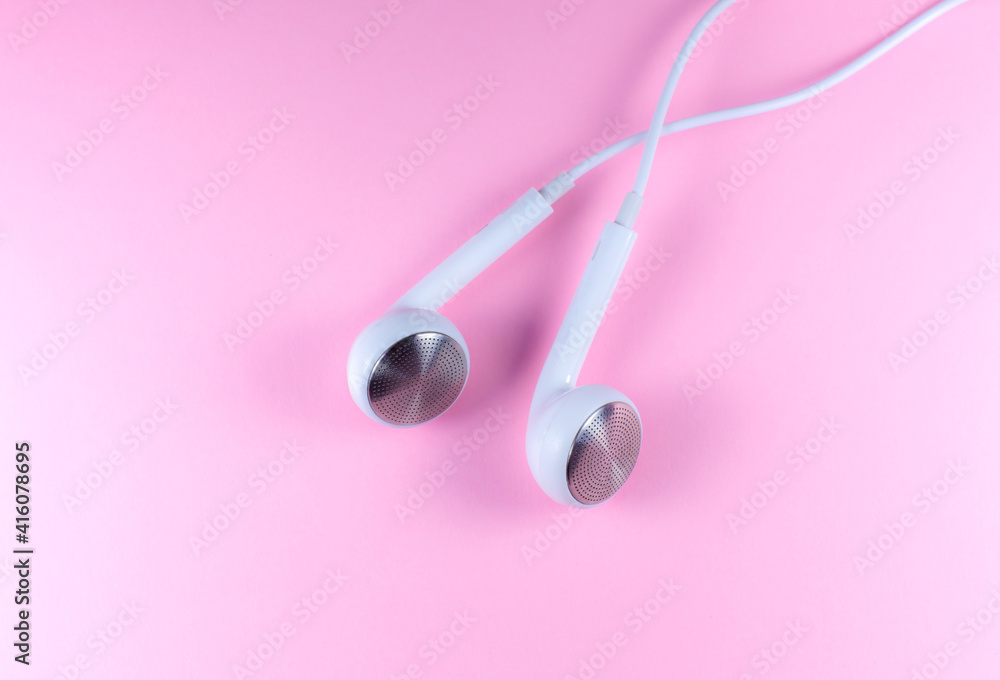 White Earphones lying on the pink background. Modern music concept. Audio technology. Close up photo. White Earphones lying on the pink background. Modern music concept. Audio technology. Close up photo.