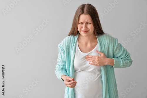 Ill pregnant young woman with pill on grey background photo