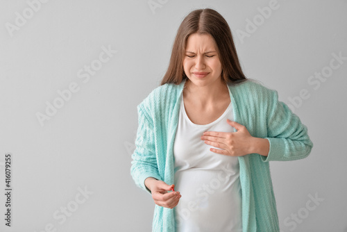 Ill pregnant young woman with pill on grey background