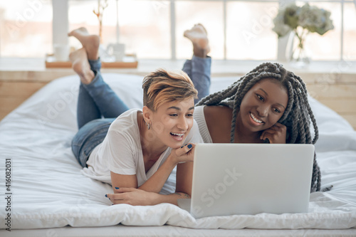Two girls lying on the bed and watching a movie on a laptop