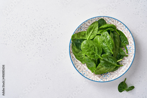 Fresh baby spinach leaves in ceramic beautiful bowl on light gray concrete background. Mock up. Top view.