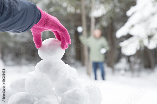 Canvas Print Original winter photograph of a woman's pink gloved hand picking up a snowball from a snowball pile for to have a snowball fight with man in the distance