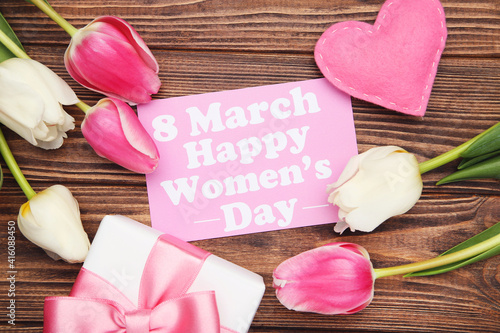 Tulip flowers, fabric heart, gift box and card with text 8 March Happy Womens Day on brown wooden background