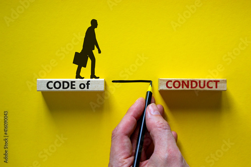 Code of conduct symbol. Wooden blocks with words 'Code of conduct'. Businessman hand. Businessman icon. Beautiful yellow background, copy space. Business and code of conduct concept. photo
