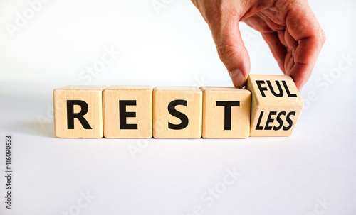Restless or restful symbol. Businessman turns the wooden cube, changes the word 'restless' to 'restful'. Beautiful white table, white background, copy space. Business and restless or restful concept.