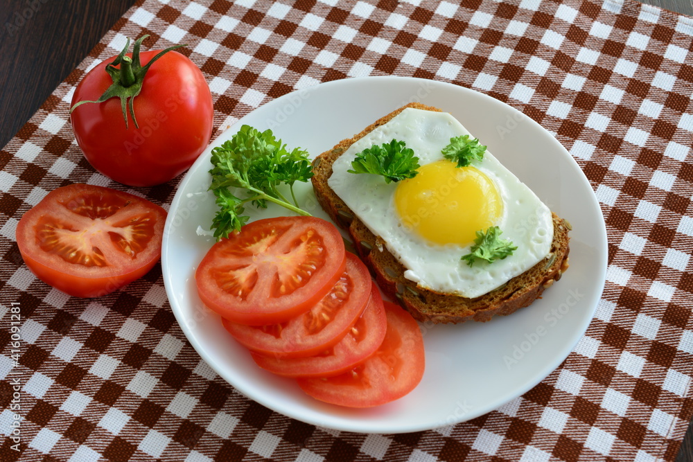sandwich with fried egg on the white plate with tomatoes and whole grain bread on the plaid tablecloth sandwich with fried egg on the white plate with tomatoes and whole grain bread on the plaid tablecloth