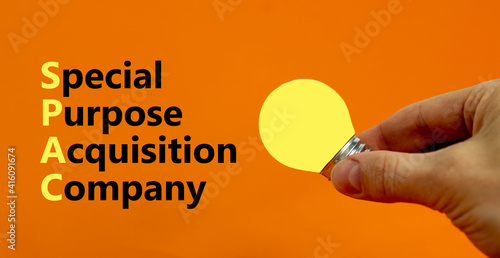 SPAC, special purpose acquisition company symbol. Word 'SPAC' on beautiful orange background, copy space. Businessman hand, light bulb. Business and SPAC, special purpose acquisition company concept. photo