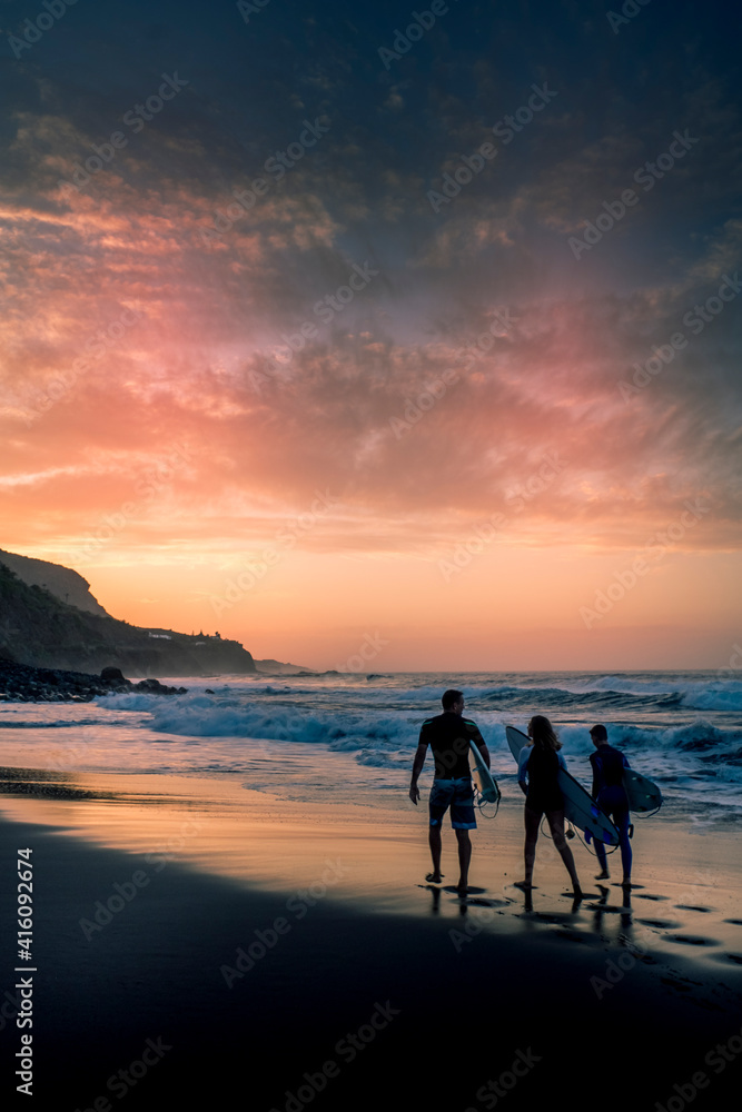 Surf group of people walk to the ocean waves to enjoy surf water sport activity in the sunset - concept of active lifestyle and summer holdiay vacation together friends