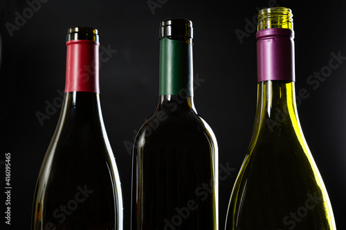 several open Bottles without wine labels stand against a dark glossy background.