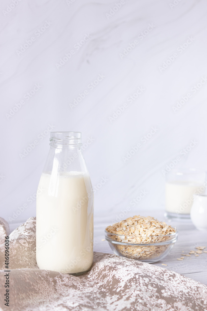 Vegetable oat milk in a glass bottle and oat flakes on a light background. Healthy drinks, vegetarianism. Side view. Vertical photo Vegetable oat milk in a glass bottle and oat flakes on a light background. Healthy drinks, vegetarianism. Side view. Vertical photo