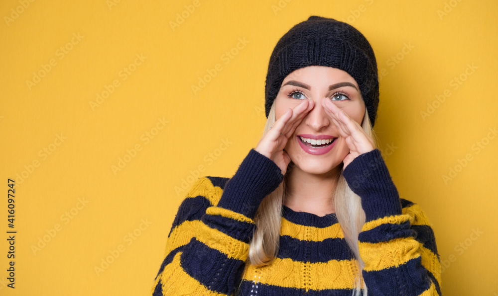 Young woman yelling, model wearing woolen cap and sweater, isolated on yellow background. Happy girl with hands on head holding Young woman yelling, model wearing woolen cap and sweater, isolated on yellow background. Happy girl with hands on head holding