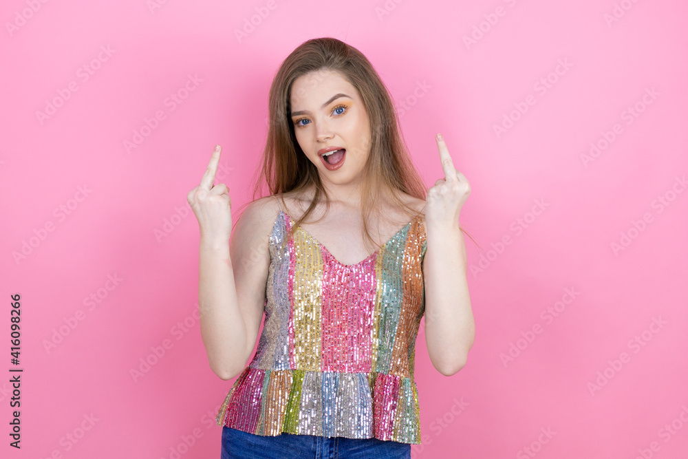Pretty redhead woman wearing a shiny top standing over pink background showing middle finger doing fuck you bad expression, provocation and rude attitude. screaming excited Pretty redhead woman wearing a shiny top standing over pink background showing middle finger doing fuck you bad expression, provocation and rude attitude. screaming excited