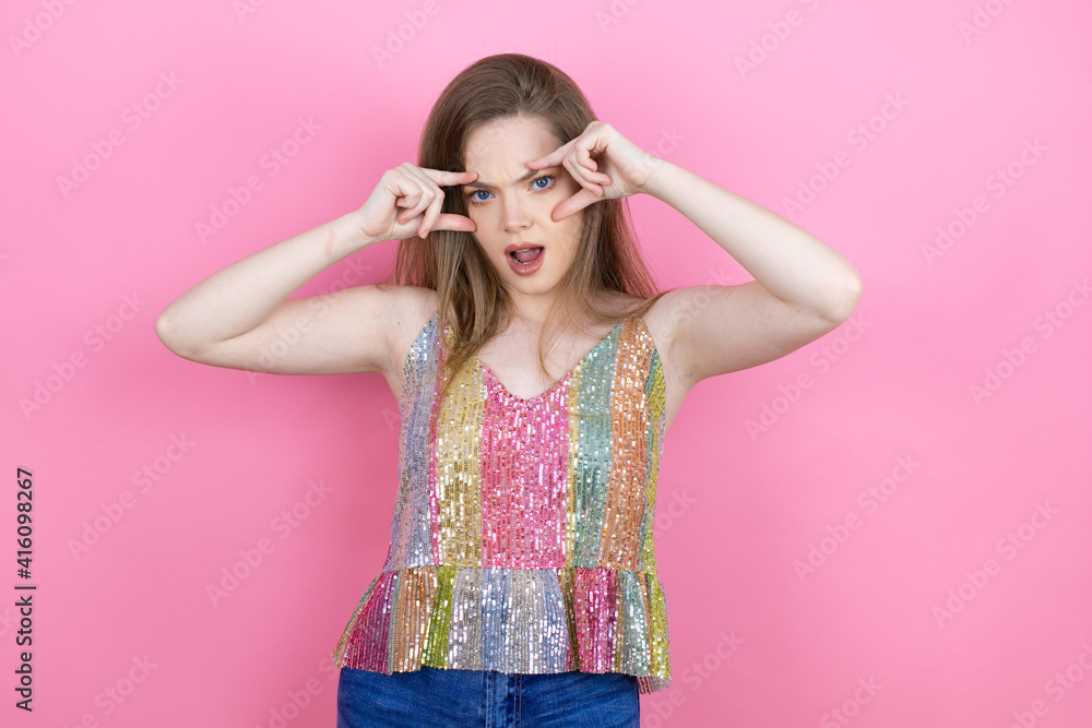 Pretty redhead woman wearing a shiny top standing over pink background Trying to open eyes with fingers, sleepy and tired for morning fatigue Pretty redhead woman wearing a shiny top standing over pink background Trying to open eyes with fingers, sleepy and tired for morning fatigue